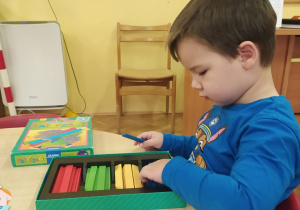 chłopiec przy stoliku bawi się kolorowymi, plastikowymi klockami - patyczakami