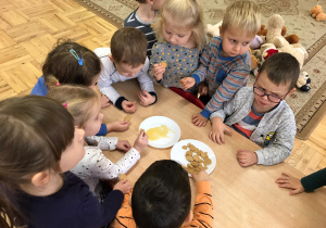 dzieci zgromadzone wokół stolika jedzą ciasteczka