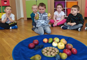 dzieci siedzą w kole, w środku leży granatowa chusta z owocami a chłopiec trzyma gruszki