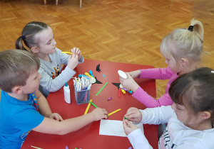 dzieci składają paski kolorowego papieru - włosy w "wachlarzyk"