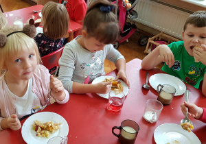 dzieci przy stoliku jedzą z talerzyków samodzielnie przygotowaną sałatkę owocową
