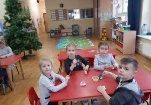dzieci przy stolikach malują farbami ozdoby na choinkę