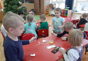 dzieci przy stolikach malują ozdoby na choinkę