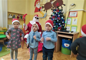 dzieci stoją i śpiewają Mikołajowi piosenkę i ilustrują ruchem