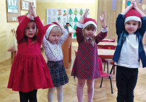dzieci w czerwonych czapkach stoją z rękami w górze - "czapeczka" i śpiewają