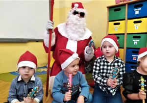 dzieci siedzą i grają na instrumentach razem z Mikołajem, który klęczy za nimi