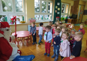 dzieci stoją przed Mikołajem, który siedzi a obok worek z prezentami