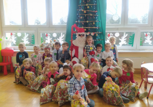 dzieci z grupy II z paczkami z Mikołajem, który trzyma dziewczynkę na kolanach