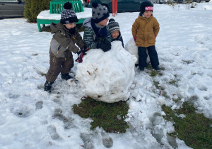 chłopcy opierają się o wielką kulę śniegu