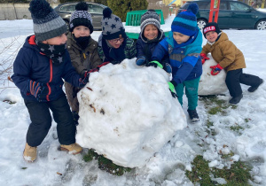 sześciu chłopców pcha wielką kulę śniegu