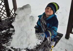 chłopiec lepi śniegowego bałwana na ławie w ogrodowej altanie