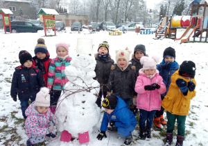 pada śnieg a grupa dzieci stoi przy bałwanie