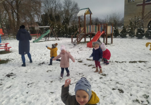 w ogrodzie dzieci biegają i rzucają śnieżkami w panią