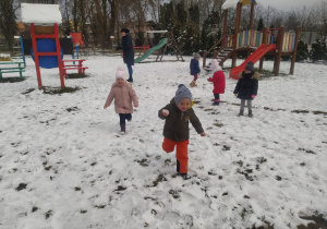 w ogrodzie dzieci biegają i rzucają się śnieżkami