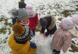 dzieci dolepiają śnieg do kuli śniężnej