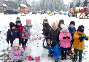 pada śnieg, w ogrodzie dzieci pozują do zdjęcia z ulepionym bałwanem,