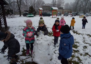 dzieci niosą kulki śniegu w rękach w stronę bałwana
