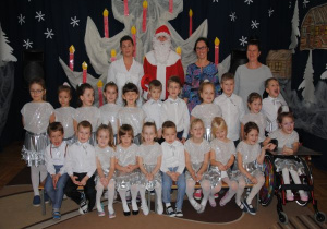 zdjęcie grupowe dzieci z gr8 w biało - srebrnych strojach z Mikołajem, opiekunką i nauczycielkami