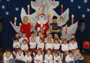 zdjęcie grupowe dzieci z gr9 w czerwono - białych strojach z Mikołajem i nauczycielkami