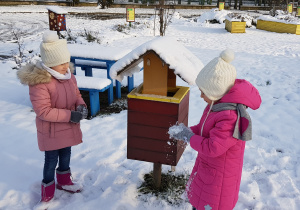 dwie dziewczynki stoją w ogrodzie i lepią śniegowe kulki