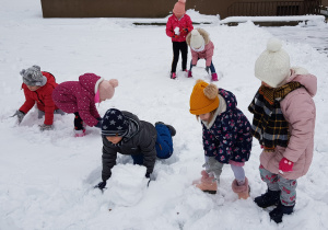dzieci w ogrodzie toczą kule śniegowe