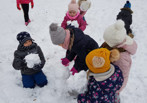 dzieci ze swoich kul śniegowych układają bałwana