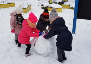 dzieci toczą wielką kulę śniegową