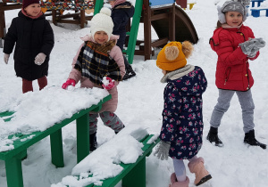 dzieci bawią się śniegiem w okolicy zielonej ławki i stolika