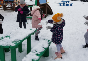dziewczynki rzucają się śniegiem w okolicy zielonej ławki i stolika