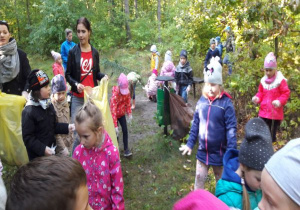nauczycielki trzymają worki a dzieci wrzucają do nich znalezione w lesie śmieci