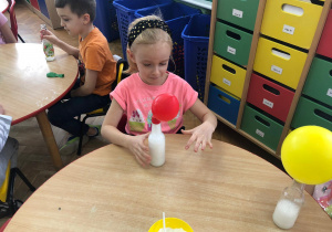 dziewczynka obserwuje jak różowy balon umieszczony na butelce rośnie