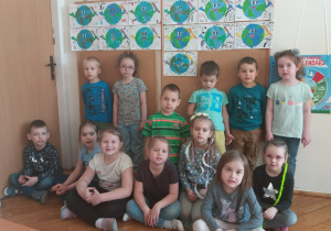 dzieci z grupy V ubrane w kolory ziemi stoją przed tablicą ze swoimi pracami o Ziemi