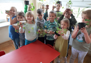 dzieci pokazują małe doniczki z posadzonymi roślinkami