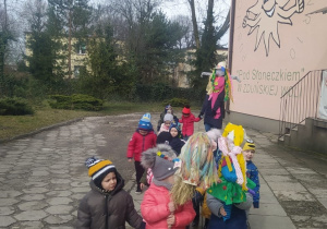 dzieci idą po chodniku przed budynkiem przedszkola z Marzannami