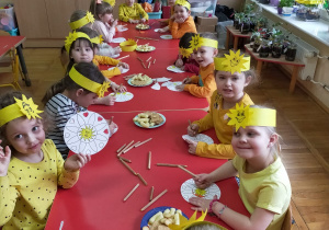dzieci w żółtych opaskach ze słoneczkami na głowach siedzą przy stoliku i kolorują obrazki - mandale ze słoneczkiem