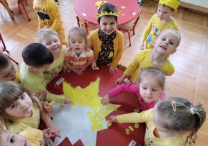 dzieci przy stoliku wyklejają żółtą bibułą duży kontur słońca
