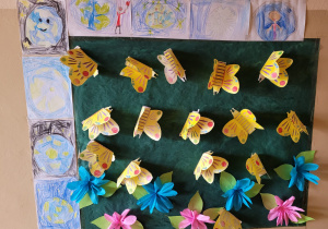prace plastyczne dzieci o Ziemi wokół pracy zbiorowej: łąka a na niej papierowe, żółte motyle i kolorowe kwiaty z bibuły