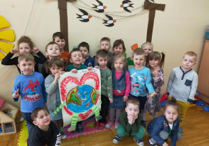 dzieci prezentują swoją plakat o Ziemi: praca malowana farbą: uśmiechnięta planeta Ziemia z doklejonymi harmonijkowymi rękami i nogami na tle wielkiego, czerwonego serca
