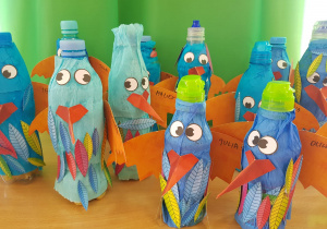 ptaki z butelki, oklejone niebieską bibułą z pomarańczowymi skrzydłami i naklejanymi papierowymi piórami, oczami oraz czerwonym dziobem