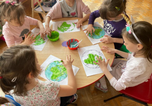 dzieci przy stolikach malują kontur Ziemi palcem i farbami: zieloną i niebieską