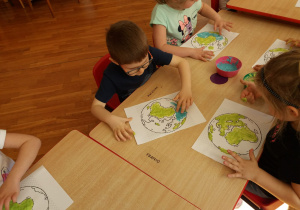 dzieci przy stolikach malują kontur Ziemi palcem i farbami: zieloną i niebieską