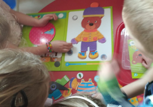 dzieci ubierają misia narysowanego na tablicy magnetycznej przykładając ubrania
