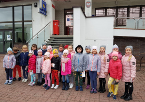 dzieci ze swoimi kartkami stoją przed budynkiem urzędu pocztowego