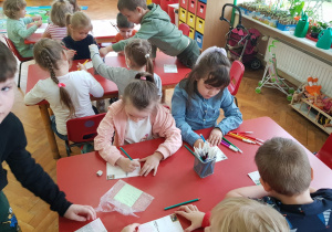dzieci przy stolikach piszą pozdrowienia i ozdabiają swoje kartki