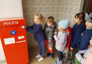 dzieci z kartkami stoją w kolejce do skrzynki pocztowej
