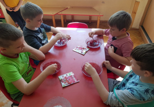 chłopcy przy stoliku mieszają w pojemnikach czerwoną galaretkę
