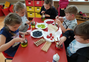 dzieci przy stoliku komponują deser dla mamy, wkładają owoce na galaretkę