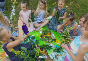 dziewczynki z grupy VI w ogrodzie, na macie, robią bukiety z kwiatów i zbóż
