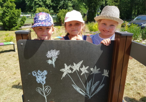 dziewczynki z grupy VI w ogrodzie, stoją za tablicą z narysowanymi kwiatami