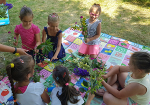 dziewczynki z grupy V w ogrodzie, na macie robią bukiety z kwiatów i zbóż
